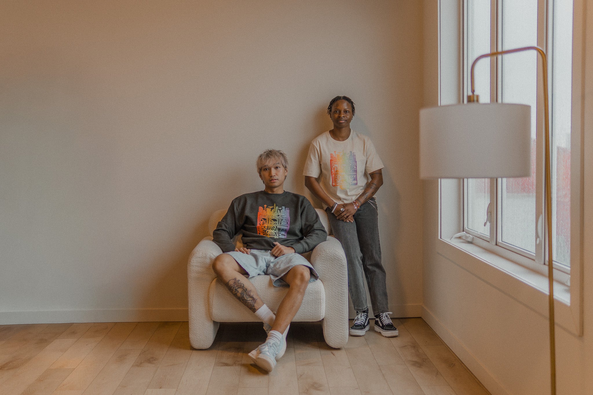 Two people sitting in a room with a large window and lamp.